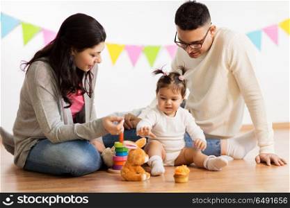 family, holidays and people concept - happy mother, father and little daughter playing with toys on birthday party. baby girl with parents playing with toys. baby girl with parents playing with toys