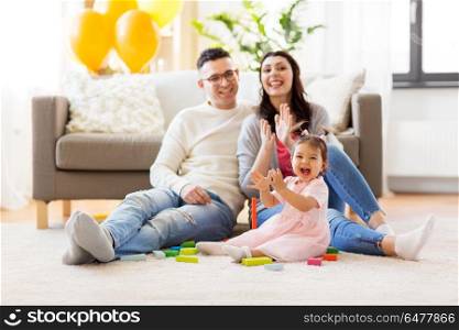family, holidays and people concept - happy mother, father and little daughter clapping hands at home. baby girl with parents clapping hands at home. baby girl with parents clapping hands at home