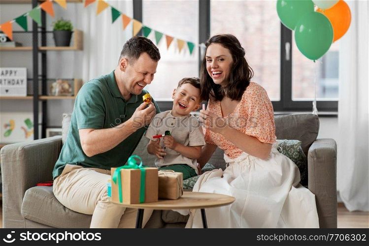 family, holidays and people concept - happy mother, father and little son with gifts and party blowers having fun and celebrating birthday at home. happy family with gifts and party blowers at home