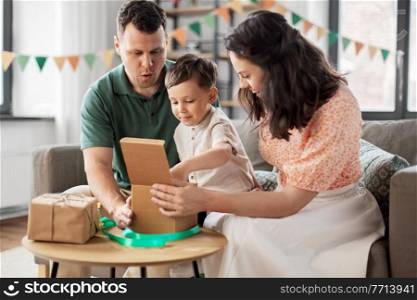 family, holidays and people concept - happy mother, father and little son opening birthday presents at home party. happy family opening birthday presents at home