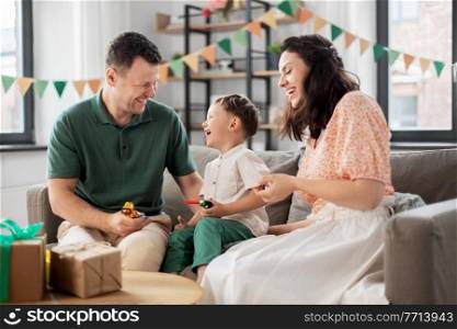 family, holidays and people concept - happy mother, father and little son with gifts and party blowers having fun and celebrating birthday at home. happy family with gifts and party blowers at home