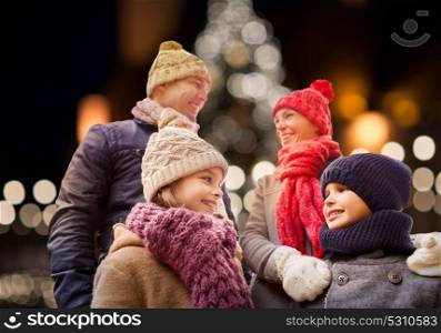 family, holidays and people concept - happy parents with kids outdoors over christmas tree lights background. happy family outdoors at christmas eve