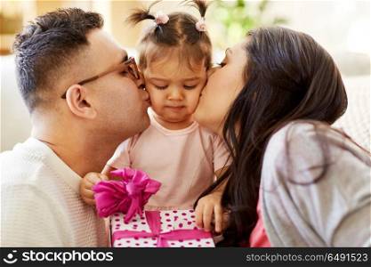 family, holidays and people concept - mother and father kissing little daughter with birthday gift. parents kissing little daughter with birthday gift. parents kissing little daughter with birthday gift