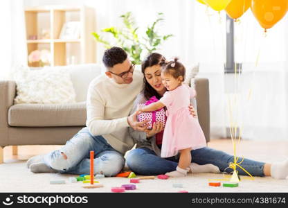 family, holidays and people concept - mother, father and happy little daughter with gift box at home birthday party. baby girl with birthday gift and parents at home . baby girl with birthday gift and parents at home