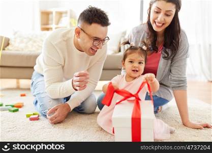 family, holidays and people concept - mother, father and happy little daughter with gift box at home birthday party. baby girl with birthday gift and parents at home. baby girl with birthday gift and parents at home