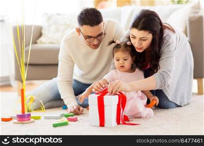 family, holidays and people concept - mother, father and happy little daughter with gift box at home birthday party. baby girl with birthday gift and parents at home . baby girl with birthday gift and parents at home