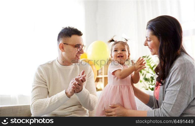 family, holidays and people concept - mother, father and happy little daughter clapping hands at home birthday party. happy baby girl and parents at home birthday party. happy baby girl and parents at home birthday party