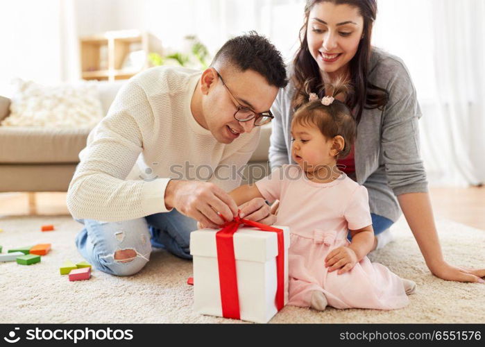 family, holidays and people concept - mother, father and happy little daughter with gift box at home birthday party. baby girl with birthday gift and parents at home. baby girl with birthday gift and parents at home