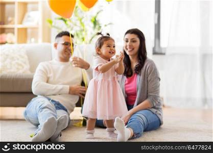 family, holidays and people concept - mother, father and happy little daughter at home birthday party. happy baby girl and parents at home birthday party. happy baby girl and parents at home birthday party