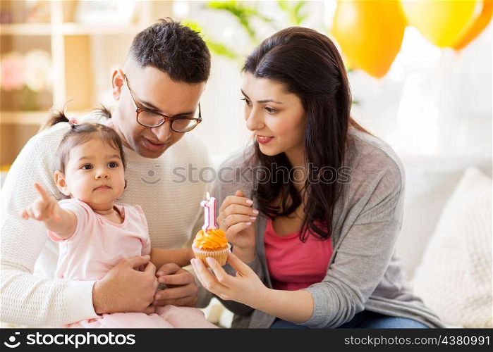 family, holidays and people concept - mother, father with cupcake and happy little daughter at home birthday party. baby girl with parents at home birthday party. baby girl with parents at home birthday party
