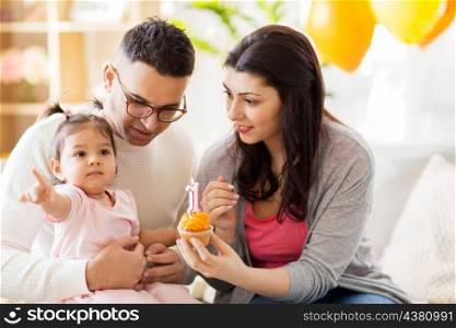 family, holidays and people concept - mother, father with cupcake and happy little daughter at home birthday party. baby girl with parents at home birthday party. baby girl with parents at home birthday party