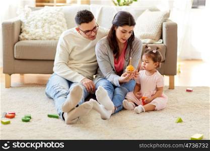 family, holidays and people concept - mother with birthday cupcake, father and happy little daughter at home party. baby girl with parents at home birthday party. baby girl with parents at home birthday party