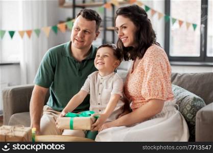 family, holidays and people concept - portrait of happy mother and father giving birthday present to little son sitting on sofa at home party. parents giving birthday present to little son