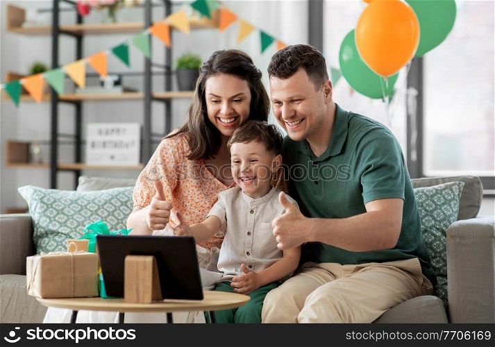 family, holidays and people concept - portrait of happy mother, father and little son with tablet pc computer and birthday gifts on table having video call at home party and showing thumbs up. family with tablet pc has video call on birthday
