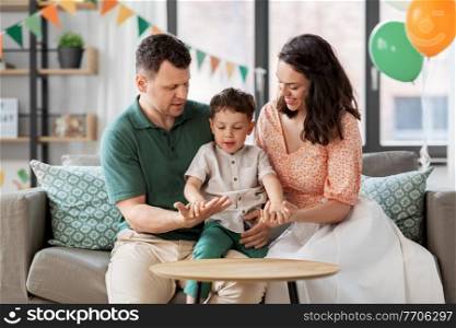 family, holidays and people concept - portrait of happy mother, father and little son sitting on sofa at home party. happy family with little son at birthday party