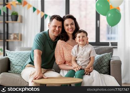 family, holidays and people concept - portrait of happy mother, father and little son sitting on sofa at home party. happy family with little son at home party