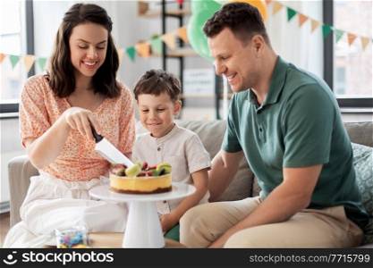 family, holidays and people concept - portrait of happy mother, father and little son with birthday cake sitting on sofa at home party. happy family with birthday cake at home