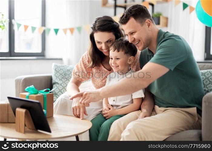 family, holidays and people concept - portrait of happy mother, father and little son with tablet pc computer and birthday gifts on table sitting on sofa at home party. happy family with tablet pc at home on birthday
