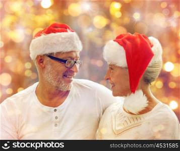 family, holidays, christmas, age and people concept - happy senior couple in santa helper hats over lights background