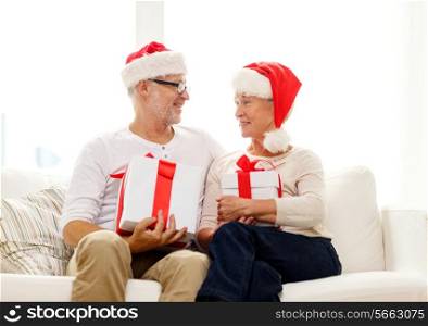 family, holidays, christmas, age and people concept - happy senior couple in santa helper hats with gift boxes at home