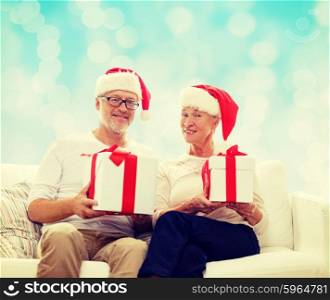 family, holidays, christmas, age and people concept - happy senior couple in santa helper hats with gift boxes over blue lights background