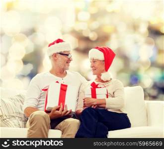 family, holidays, christmas, age and people concept - happy senior couple in santa helper hats with gift boxes over lights background