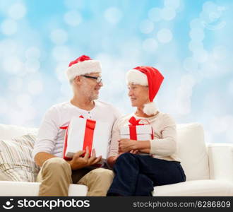 family, holidays, christmas, age and people concept - happy senior couple in santa helper hats with gift boxes over blue lights background