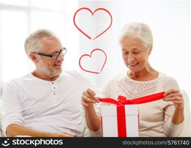 family, holidays, christmas, age and people concept - happy senior couple opening gift box over white room background with red heart shapes