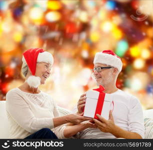 family, holidays, christmas, age and people concept - happy senior couple with gift box over red lights background
