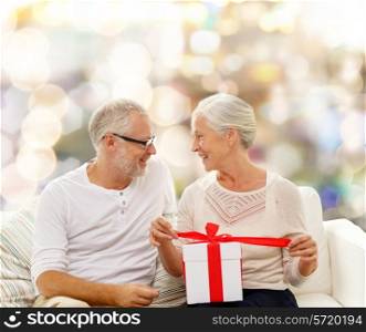 family, holidays, christmas, age and people concept - happy senior couple with gift box over lights background