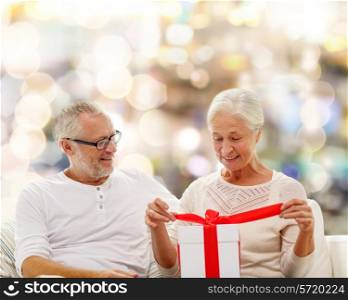 family, holidays, christmas, age and people concept - happy senior couple with gift box over lights background