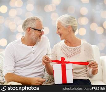 family, holidays, christmas, age and people concept - happy senior couple with gift box over holidays lights background