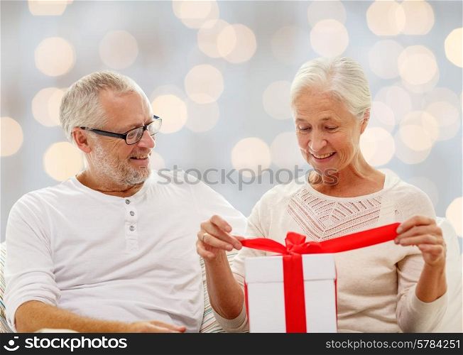 family, holidays, christmas, age and people concept - happy senior couple with gift box over holidays lights background