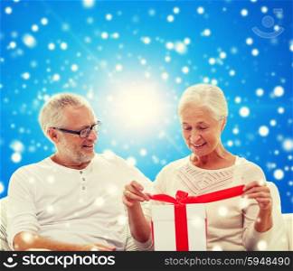 family, holidays, christmas, age and people concept - happy senior couple with gift box over blue snowy background