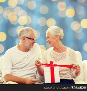 family, holidays, christmas, age and people concept - happy senior couple with gift box over blue lights background