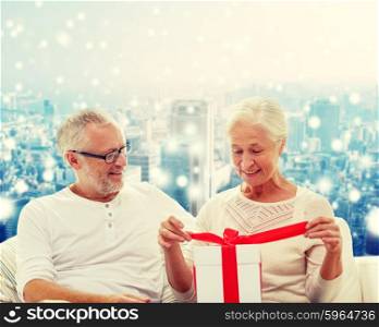 family, holidays, christmas, age and people concept - happy senior couple with gift box over snowy city background