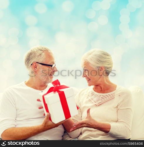 family, holidays, christmas, age and people concept - happy senior couple with gift box over blue lights background