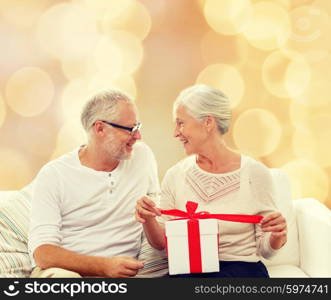 family, holidays, christmas, age and people concept - happy senior couple with gift box over beige lights background