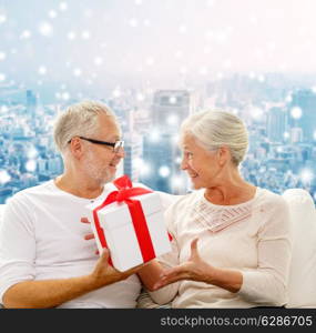 family, holidays, christmas, age and people concept - happy senior couple with gift box over snowy city background