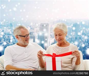 family, holidays, christmas, age and people concept - happy senior couple with gift box over snowy city background