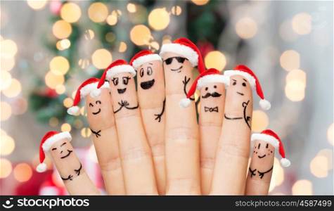 family, holidays, christmas and body parts concept - close up of fingers with smiley faces and santa hats over lights background