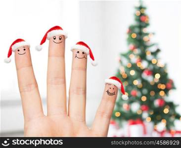 family, holidays, christmas and body parts concept - close up of hand with four fingers in santa hats with smiley faces over tree lights background