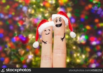 family, holidays, christmas and body parts concept - close up of two fingers with smiley faces and santa hats over lights background