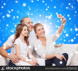 family, holidays, christmas technology and people concept - smiling mother, father and little girl making selfie with camera over blue snowy background