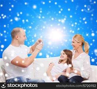family, holidays, christmas technology and people concept - smiling mother, father and little girl with camera over blue snowy background