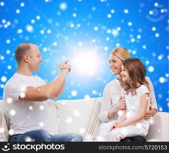 family, holidays, christmas technology and people concept - smiling mother, father and little girl with camera over blue snowy background