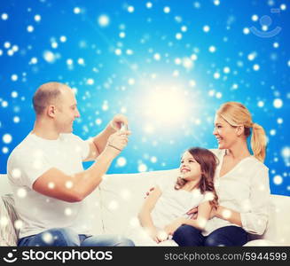 family, holidays, christmas technology and people concept - smiling mother, father and little girl with camera over blue snowy background