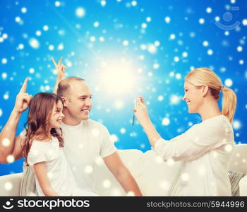 family, holidays, christmas technology and people concept - smiling mother, father and little girl with camera over blue snowy background