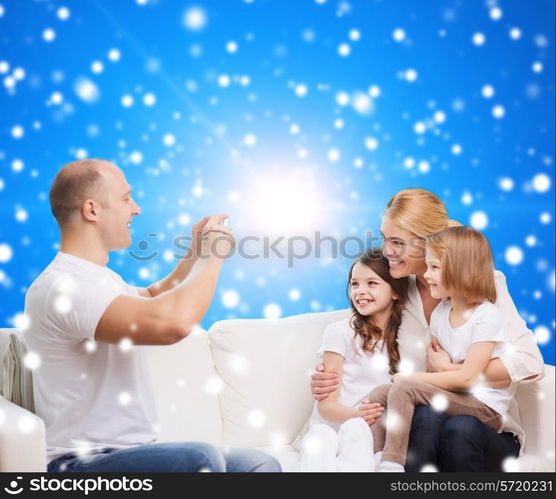 family, holidays, christmas technology and people - smiling mother, father and little girls with camera over blue snowy background