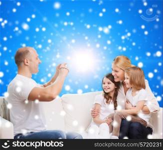 family, holidays, christmas technology and people - smiling mother, father and little girls with camera over blue snowy background